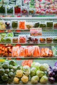 Person arranging leafy greens, berries, carrots, and tomatoes in refrigerator drawers and countertop containers.