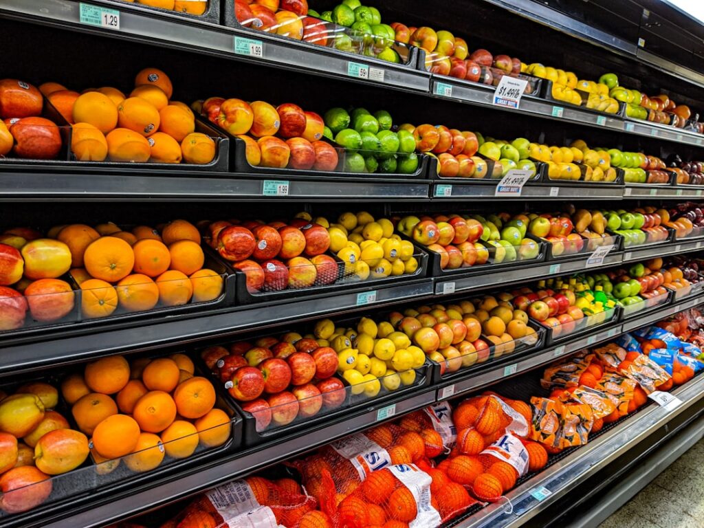 A person examining apples and leafy greens under bright grocery store lighting.