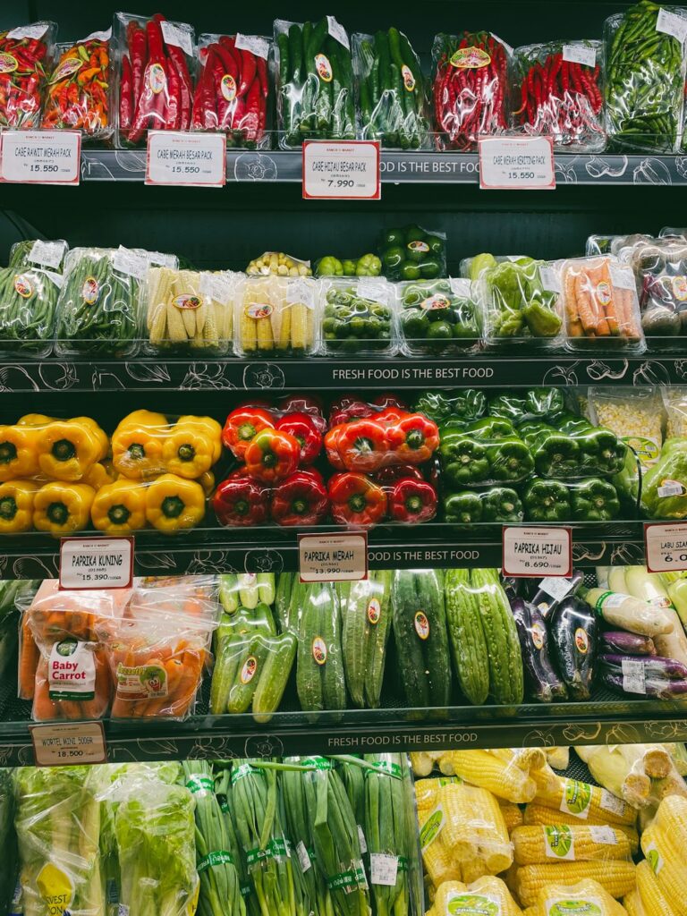 A person selecting apples and leafy greens from side-by-side organic and non-organic produce bins in a grocery store.