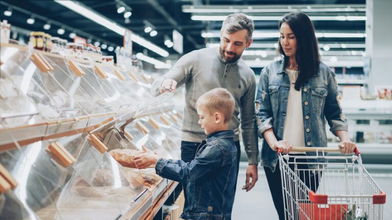 Parents and children organize groceries and prepare simple ingredients together at a kitchen table.